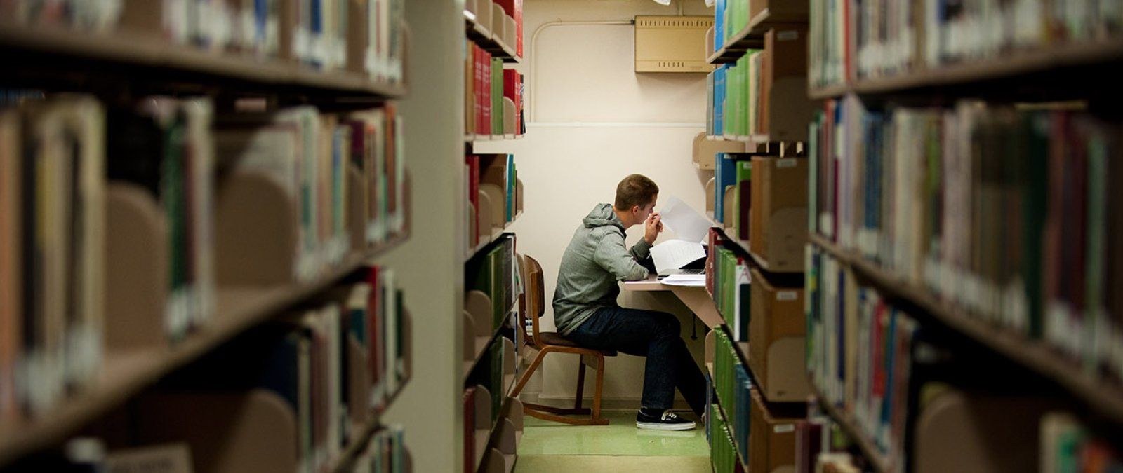 A male student sits studying at a long row of library stacks