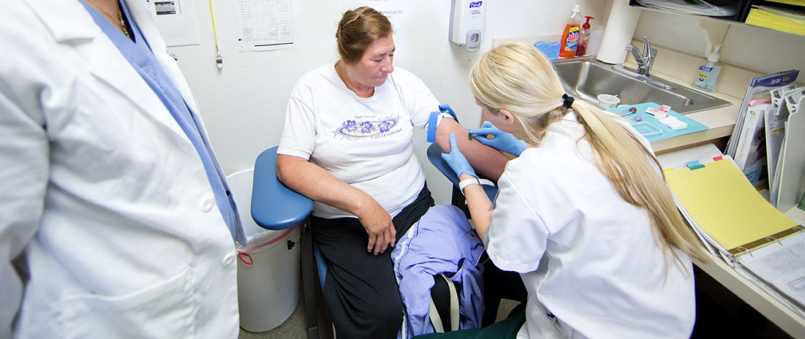 A student nurse leans over an older woman arm as she prepares the woman for a blood draw