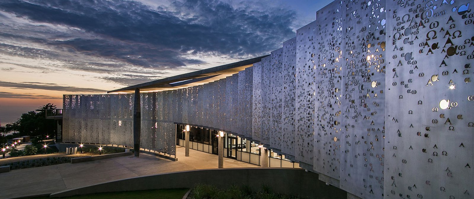 The alpha and omega metal pane wall sloping outward toward the twilight sky