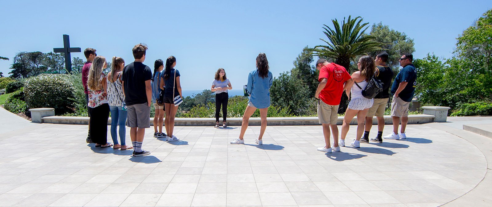 A PLNU student speaks in front of the campus cross to a group on a campus tour.