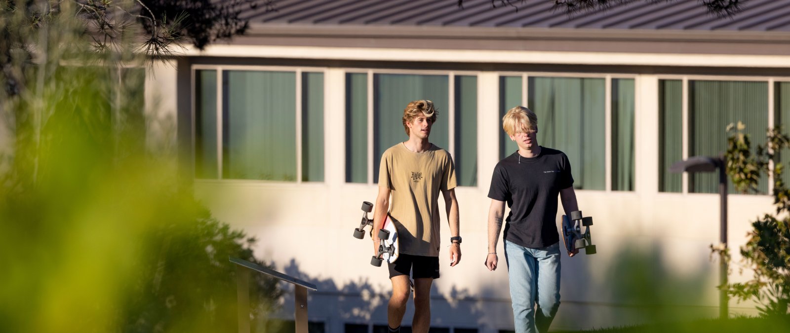 two students holding skateboards walking in front of draper hall