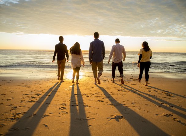 People walk towards the ocean and sunset