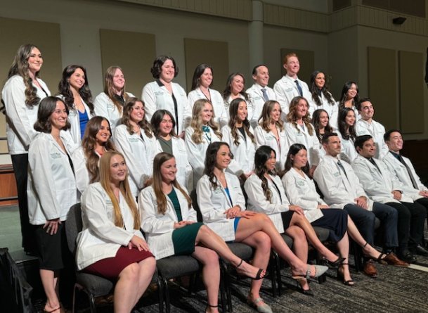 Group of students sit in rows in their white coats 