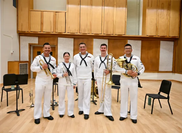 five brass musicians in navy band uniform holding their instruments