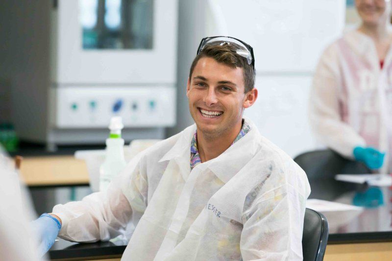 Male PLNU student in lab coat and glasses smiles