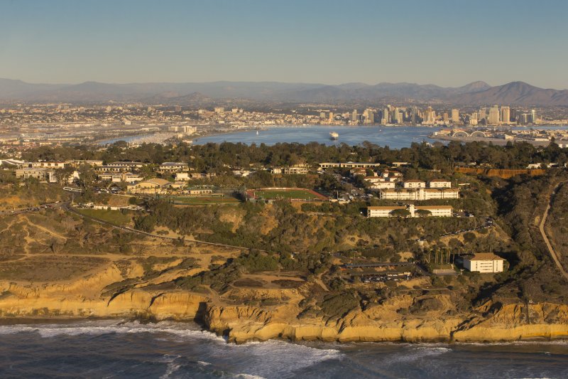 Aerial view of Point Loma campus when facing inland. Sunset cliffs, university landscape, including San Diego city skyline all included in picture taken from sky.