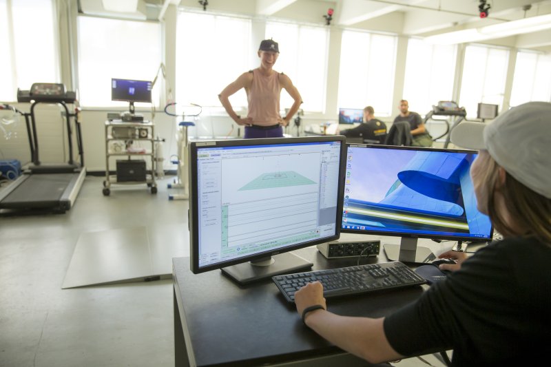 A grad student in PLNU's Integrative Wellness program sits behind a computer monitor. The monitor is displaying charts that recorded the movement of another female student who is standing in front of her.