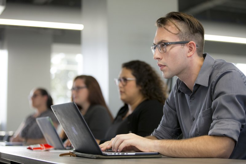 PLNU student typing notes on laptop during class lecture.