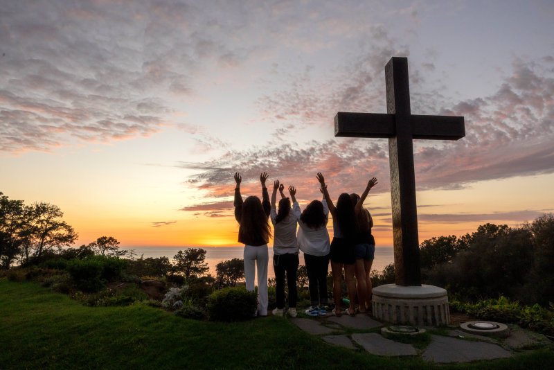 Students raise hands in joy by the PLNU cross