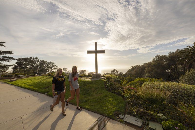 Two female students are discussing their vocational calling while walking by a cross on PLNU's campus.