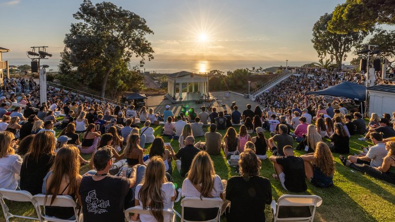 Image of PLNU community sitting and facing sunset along Pacific Ocean at the Greek Amphitheater for Welcome Week event.