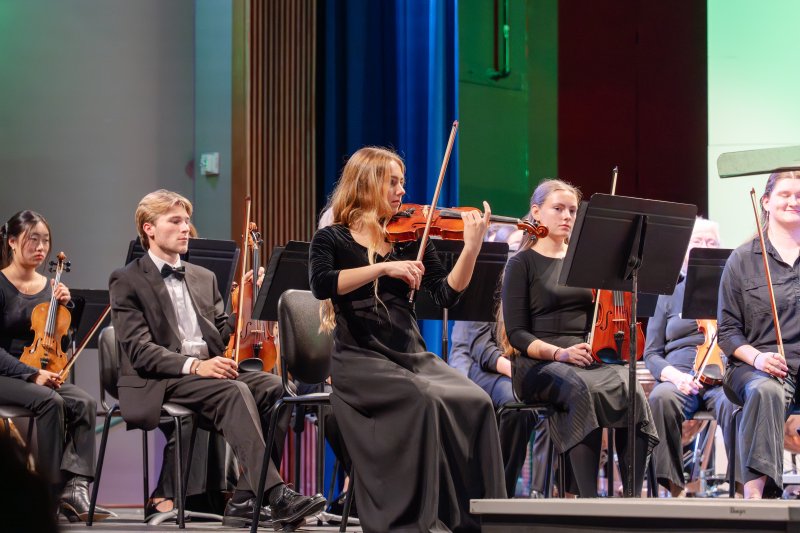 female student playing violin amongst orchestra