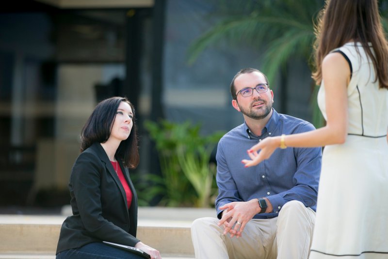 As leaders, we can cripple our organizations if we allow our teams to remain stagnant in their current patterns, pictured is a woman talking to two individuals who are listening intently. 