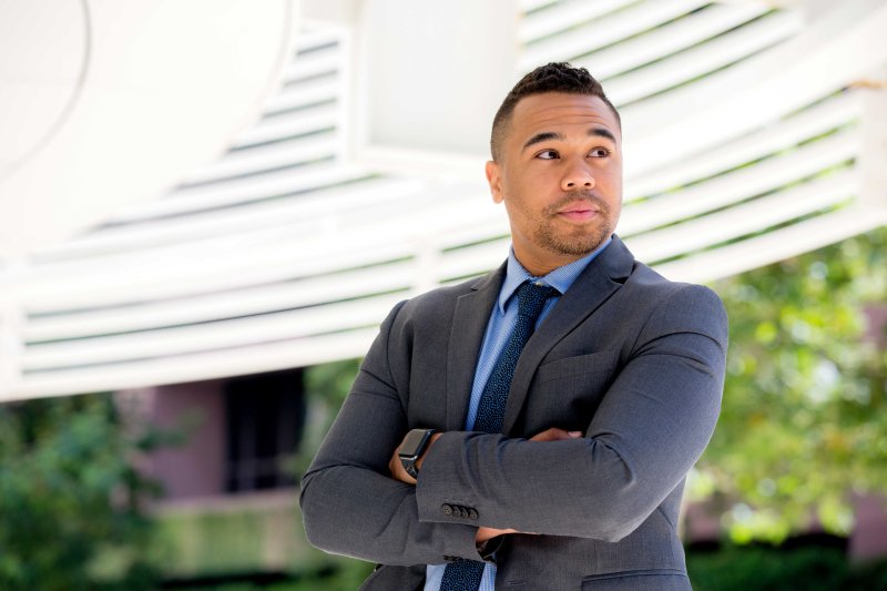 A man in business attire crosses his arms and looks confident