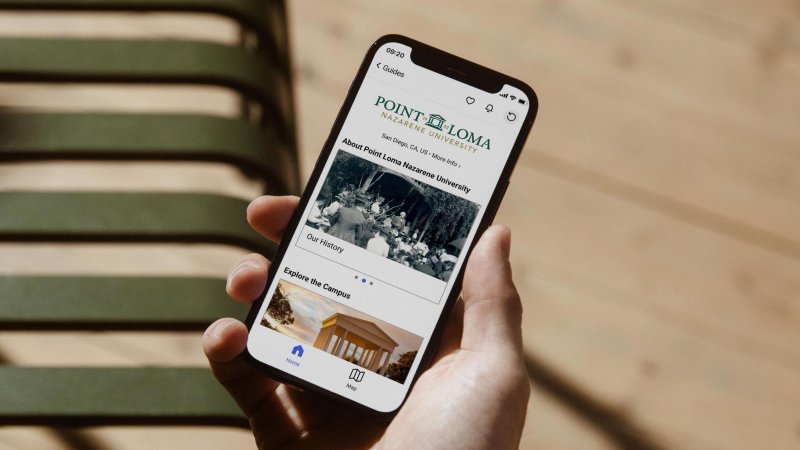 Hand holding a smartphone displaying the Bloomberg Connects application for Point Loma Nazarene University featuring campus information and navigation.
