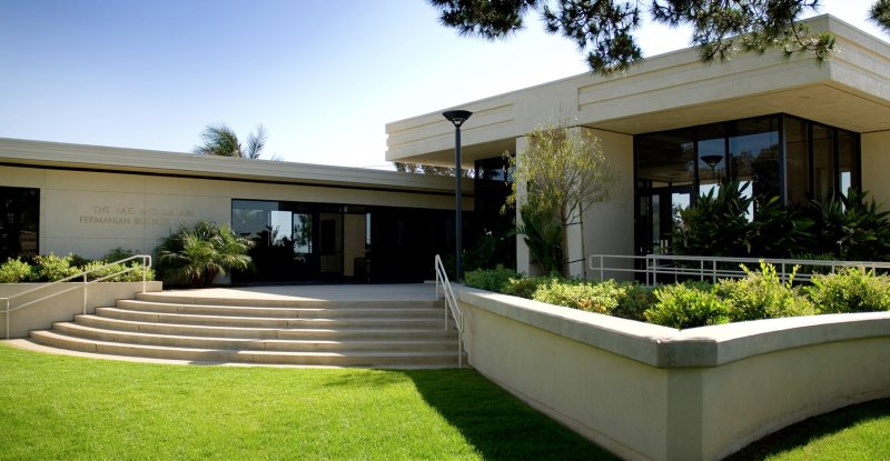 A green lawn gives way to several steps and a rectangular concrete and glass building.