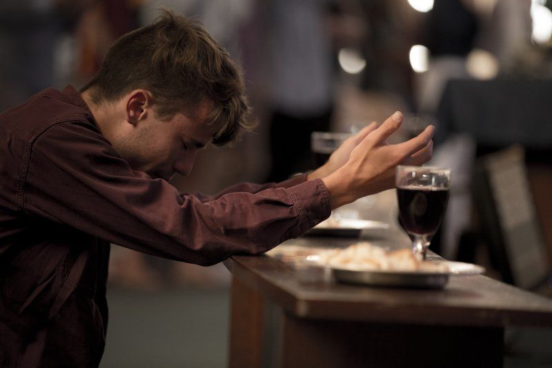 A man in a maroon button down is kneeling in front of an altar. His head is bowed and his arms are extended in prayer.