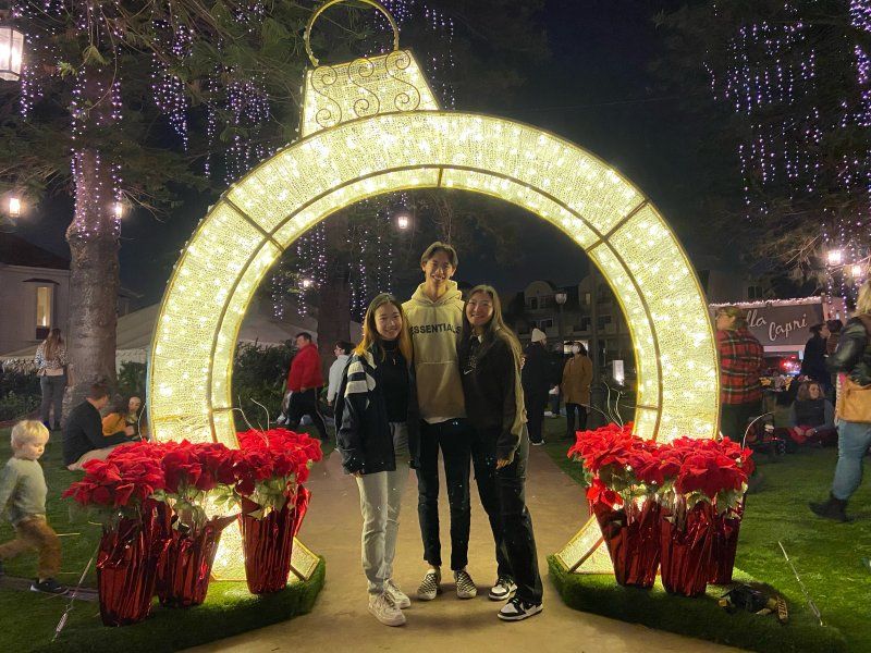 Students smile under an arch of Christmas lights