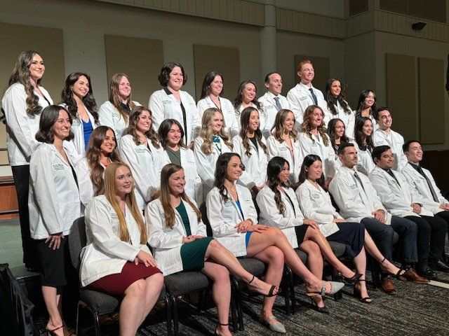 Group of students sit in rows in their white coats 