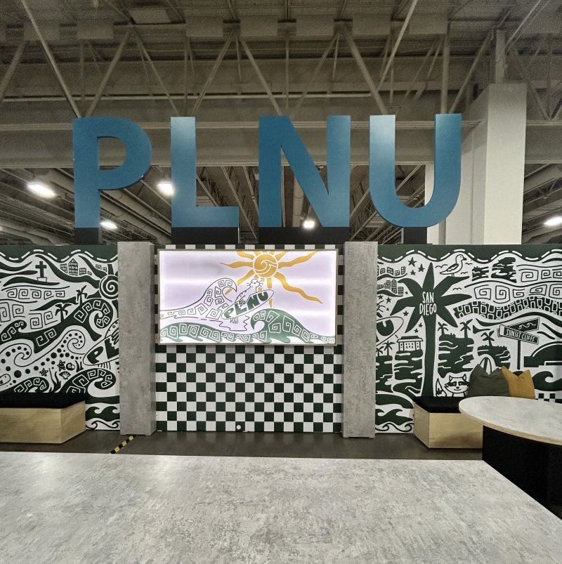 PLNU's vendor set up at the Nazarene Youth Center Conference in 2026 with the university's logo sitting above the set up with Loma graphics along the wall and a seating area for visitors.