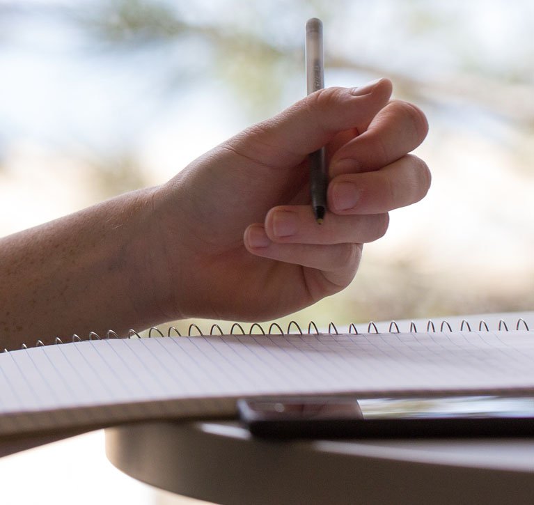 Hand holding a pencil poised to take notes on a spiral-bound notebook