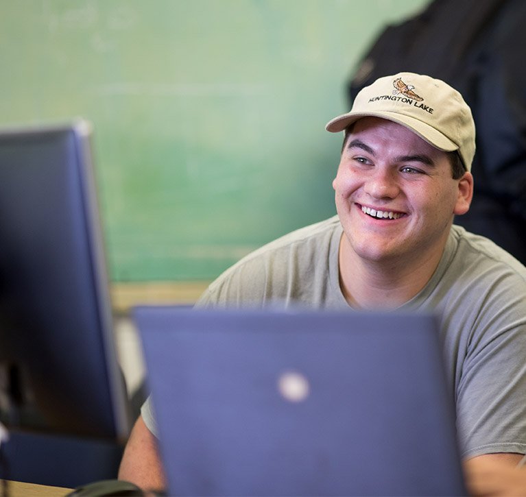 Student smiles while seated behind a computer