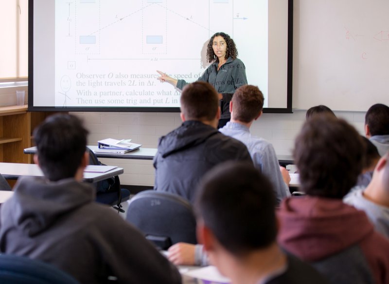 A professor teaches her class using a projector screen.