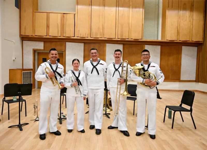 five brass musicians in navy band uniform holding their instruments