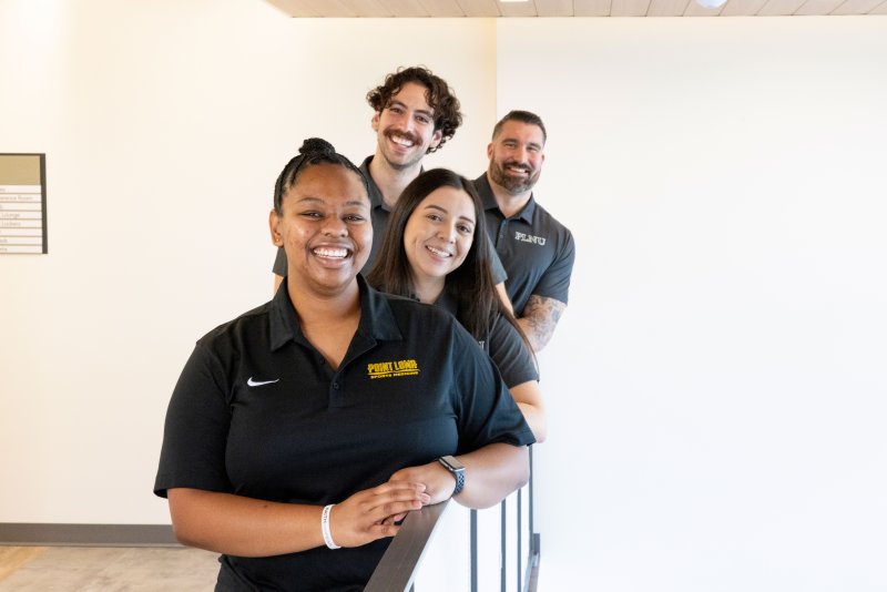 Four students smiling for a photo while leaning on a railing 