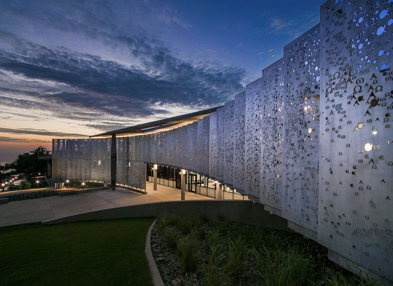 The alpha and omega metal pane wall sloping outward toward the twilight sky