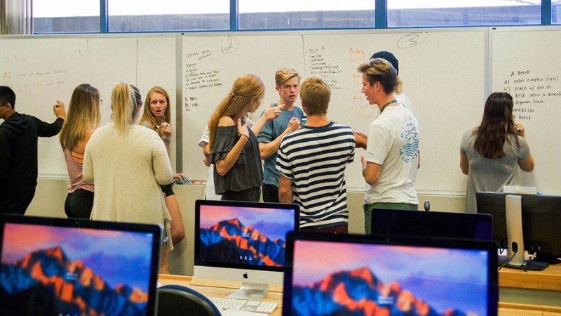 A class of students write on the front board and discuss a project.