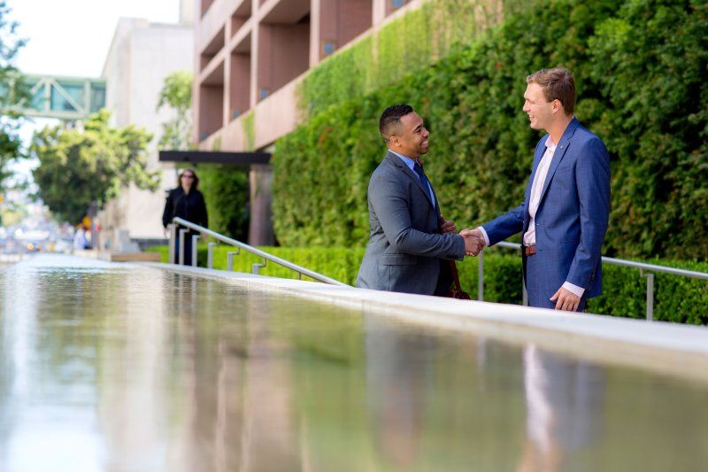 two men in suits shaking hands near a pond of water