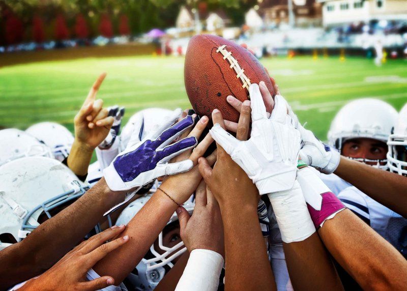 A football team raises the ball and comes together in a huddle