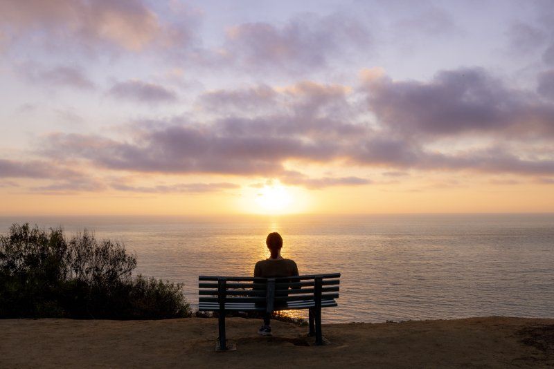 A male sits alone on a bench on Sunset Cliffs. He is looking at the sunset.