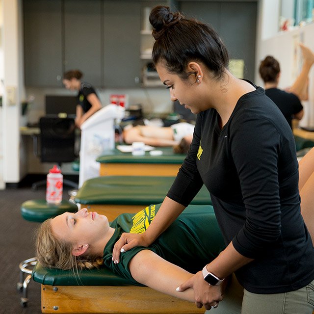 A female trainer helps a PLNU volleyball player stretch before practice.