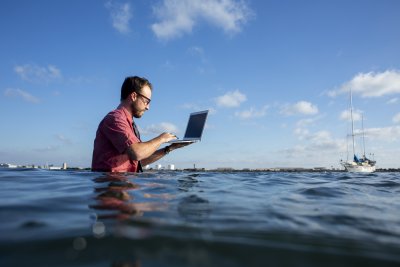 PLNU student posing for entertaining photo in San Diego bay with laptop above ocean.