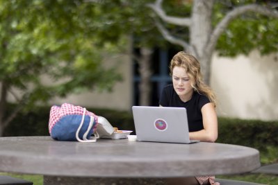 PLNU student typing on laptop outside on campus. 