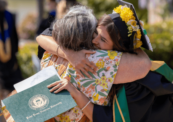 Graduating PLNU student hugging parent after receiving college diploma