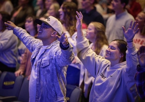 Undergraduate students in chapel with their arms raised