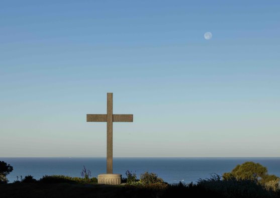 PLNU's cross overlooking the Pacific Ocean beneath a clear blue sky with the moon visible above.