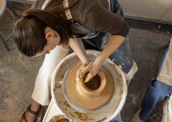 PLNU student shaping a clay vessel on a pottery wheel during a ceramics studio class.