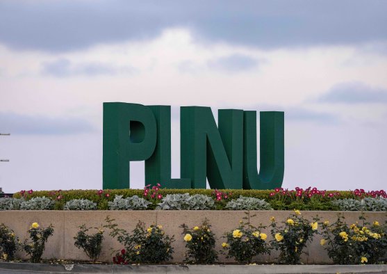 Large green PLNU letters displayed in a landscaped flower bed at the university entrance.