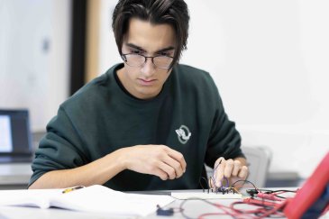 PLNU engineering student assembling and testing an electronic circuit on a breadboard during a lab exercise.