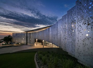 The alpha and omega metal pane wall sloping outward toward the twilight sky
