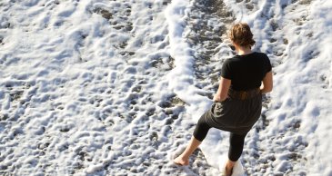 A ariel perspective of a PLNU student walking through the waves on the beach.