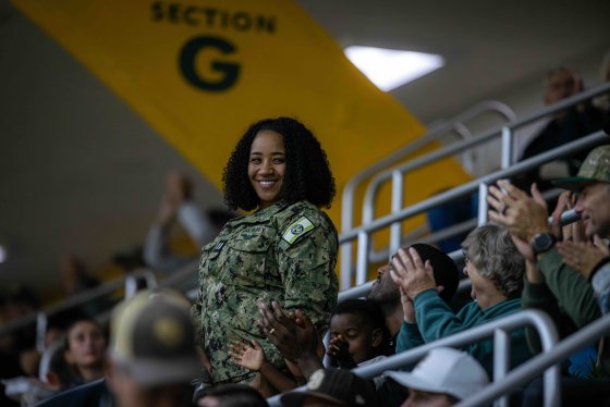 Female veteran stands in the grandstands of the Gold Gymnasium with attendees applauding around her.